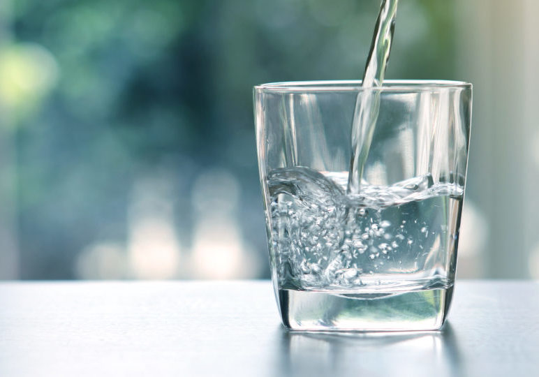 Close up pouring purified fresh drink water from the bottle on table in living room