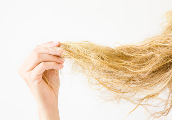 Woman's hand holding wet, blonde, tangled hair after washing on